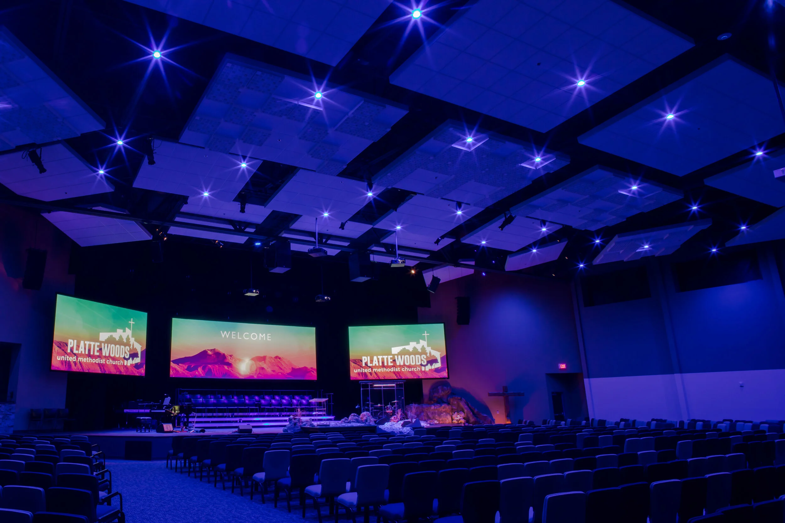 DMX RGBW LED house lights creating a serene and dramatic blue atmosphere inside a modern church sanctuary with empty seats and stage.